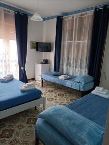 zwei Betten in einem Zimmer mit blauen Vorhängen und einem Fernseher in der Unterkunft Domus Hera in Capaccio-Paestum