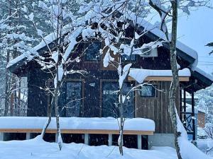 a house covered in snow in front of two trees at The Misorano Cottage in Hakuba