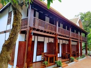 un edificio con balconi e tavoli in legno e un albero di Villa Kee Lee Hotel 1 a Luang Prabang