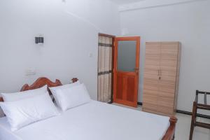 a bedroom with a white bed and a wooden door at Sun See Villa Hikkaduwa in Hikkaduwa