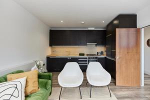 una cocina con 2 sillas blancas y un sofá verde en The Wembley Hideaway - Bright 2BDR Flat en Londres