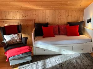 Una cama con almohadas rojas y una silla en una habitación en Ferienwohnung Bergblick am Rande der Wildnis, en Sibratsgfäll