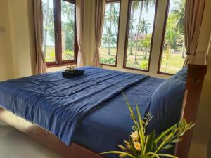 a bed with a blue comforter in a bedroom with windows at Links Sunset Beach House in Amphoe Koh Samui