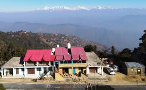 a house with a red roof with mountains in the background at Nature Valley Homestay Shaukiyathal in Panuānaula +43 photos