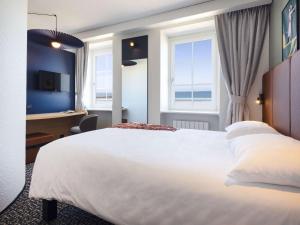 una habitación de hotel con una gran cama blanca y ventanas en ibis Saint Malo Plage, en Saint-Malo