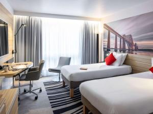 a hotel room with two beds and a desk at Novotel Edinburgh Centre in Edinburgh