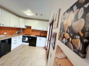 una cucina con armadi bianchi e un dipinto sul muro di Happy Sandy Feet - Modern, Cozy & Warm Holiday Home with Lovely Sea Views in Youghal`s Heart - Top-Notch Electric Heaters - Long Term Price Cuts a Youghal