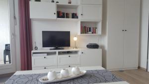 ein weißes Wohnzimmer mit einem TV und einem Tisch in der Unterkunft Strandhotel Wohnung 30 in Dahme