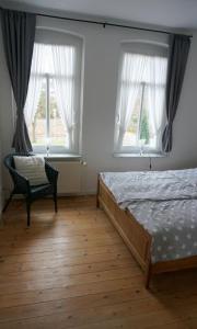 a bedroom with a bed and a chair and two windows at Villa Baltica Wohnung 02 in Dahme