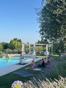 a group of people sitting on the grass by a pool at La Maggiolina Country House in Montelabbate