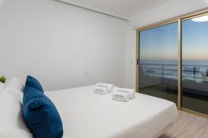 1 cama blanca con almohadas azules y balcón en OBSIDIAN Mirador del Oceano en Puerto de Santiago