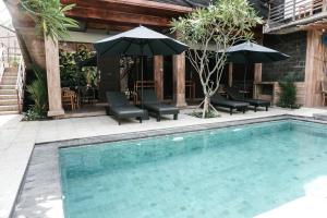 a swimming pool with chairs and umbrellas next to a building at Olas homestay bali in Uluwatu