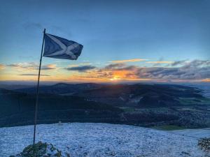 a blue flag on top of a mountain with the sunset at Braeside Innerleithen Apartment in Innerleithen