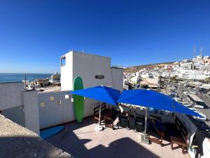 um pátio com guarda-sóis e cadeiras azuis e o oceano em Surf Taliouin Appartment Taghazout em Taghazout