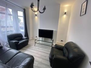 a living room with black leather furniture and a flat screen tv at Spacious 3 Bed House London in Thornton Heath