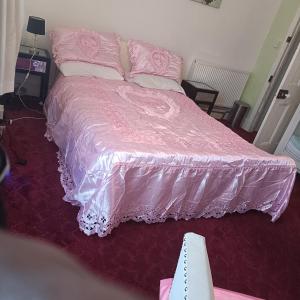 a pink bed with a pink comforter and pillows at Alysguesthub in London