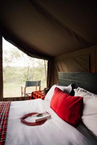 a bed with a red pillow and a book on it at Olimba Mara Camp in Mara Simba