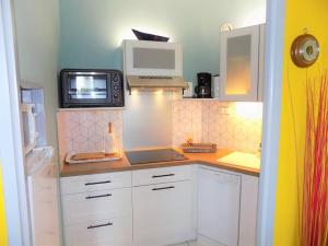 una pequeña cocina con armarios blancos y microondas en Vaux sur Mer - Quartier PONTAILLAC - APPARTEMENT - PISCINE COLLECTIVE, en Vaux-sur-Mer