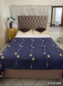 Una cama con un edredón azul con flores amarillas. en Cantinho do SOSSEGO, a 2 km da praia de Itapuã, no centro da cidade, wifi, ideal para CASAL en Vila Velha
