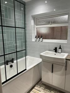 La salle de bains est pourvue d'un lavabo, d'une baignoire et d'un miroir. dans l'établissement Cozy 3 Bed Home in Halifax with Secure Parking - Long & short stays welcome!, à Halifax