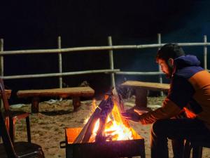 Un homme assis autour d'un feu devant dans l'établissement The White Season Residency, à Narkanda