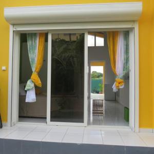 a room with sliding glass doors with yellow curtains at Jeune Tournesol (Bungalow neuf) in Sainte-Anne