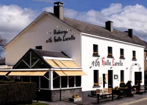 Un bâtiment blanc avec des personnes assises sur des bancs devant lui dans l'établissement Auberge la Hutte Lurette, à Paliseul