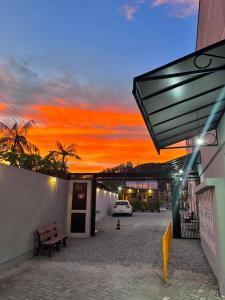 una puesta de sol detrás de un edificio con un banco y un coche en Residencial Wall Paraíso, en Itapema