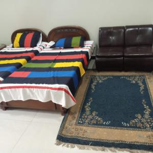 two beds in a room with a couch and a rug at N N Guests Palace in Islamabad