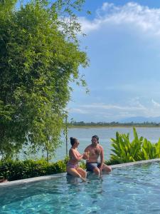 un hombre y una mujer sentados en una piscina en Nghê Prana Villa & Spa Hoi An, en Hoi An