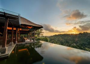 ウブドにあるMandapa, a Ritz-Carlton Reserveの夕日を背景に見えるリゾートのプール