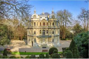 ein altes Gebäude in einem Park mit Bäumen und Sträuchern in der Unterkunft Studio entre Paris et Versailles in Le Port-Marly