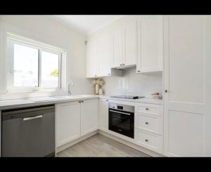 cocina blanca con armarios blancos y ventana en Little Manly 3 bedroom Oasis en Sídney