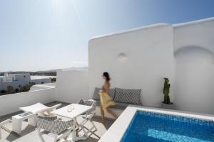 a woman sitting on a balcony next to a swimming pool at White Dunes Luxury Boutique Hotel in Santa Maria