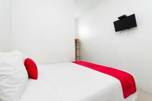 1 cama blanca con almohadas rojas y TV en la pared en RedDoorz Syariah near RSUD Zainoel Abidin Banda Aceh en Banda Aceh