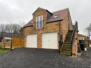una casa de ladrillo con 2 puertas de garaje y una escalera en Roseberry Barn, Bullamoor, Northallerton, North Yorkshire, en Brompton