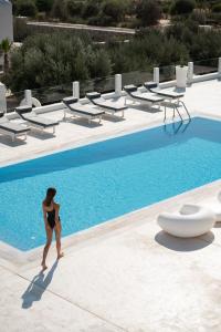 a woman in a bikini standing next to a swimming pool at White Dunes Luxury Boutique Hotel in Santa Maria