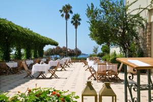 a patio with tables and chairs and palm trees at Hotel Palas in Petrovac na Moru