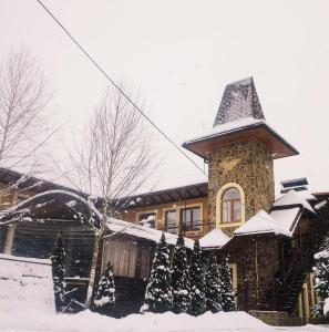 a snow covered house with a building with a tower at Minihotel Zolotoe Runo in Ploskoye