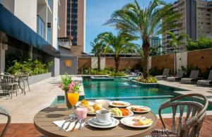 una mesa con comida y bebida en un balcón con piscina en Hotel Rafain Centro, en Foz do Iguaçu