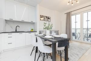 une cuisine et une salle à manger avec une table noire et des armoires blanches dans l'établissement Cozy Apartments Warsaw Wola Kasprzaka by Noclegi Renters, à Varsovie