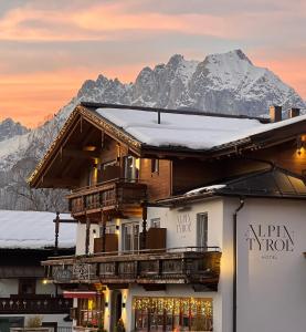 un edificio con nieve en el techo con montañas en el fondo en Hotel Alpin Tyrol - Kitzbüheler Alpen, en Sankt Johann in Tirol