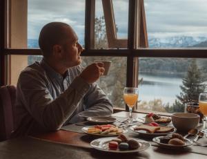 Um homem sentado à mesa a beber um copo de sumo de laranja. em Boutique Hotel & Spa Bosque del Nahuel em San Carlos de Bariloche