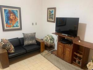 sala de estar con sofá negro y TV de pantalla plana en Casa Beira Mar - Enseada dos Golfinhos, en Itamaracá