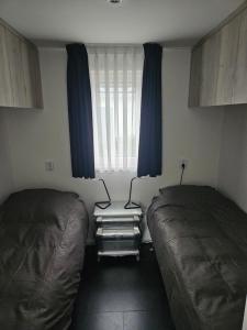 a bedroom with two beds and a window with blue curtains at Chalet Veluwemeerzicht Elburg in Biddinghuizen