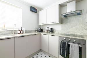 a white kitchen with white cabinets and a sink at Olive Tree Townhouse, with parking in Whitstable