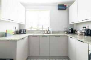 a white kitchen with white cabinets and a window at Olive Tree Townhouse, with parking in Whitstable