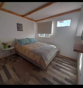 a bedroom with a bed and a table and two windows at Loft a pasos de la playa in La Serena