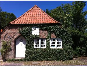 una pequeña casa de ladrillo con puerta blanca y ventanas en Doktors Hus, en Oldenswort