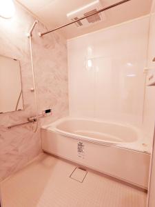 La salle de bains blanche est pourvue d'une baignoire et d'un miroir. dans l'établissement Rosenheim Tokyo Shinjuku Okubo, à Tokyo